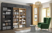 Moderne Wohnzimmeransicht mit einem großen, grauen Mehrzweckschrank und einem offenen Holzregal, gefüllt mit Büchern und Aufbewahrungsboxen. Ein grüner Sessel und ein kleiner runder Tisch stehen vor einem großen Fenster mit Vorhängen. Perspektive: Frontal