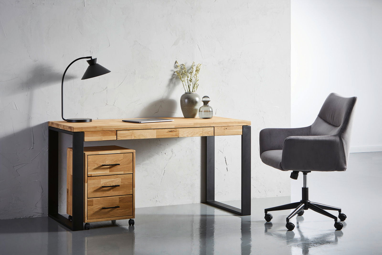 Carryhome Drehstuhl MALAGA Moderner Drehstuhl in Grau, seitliche Perspektive, neben einem Schreibtisch mit Holzplatte und schwarzem Metallgestell.