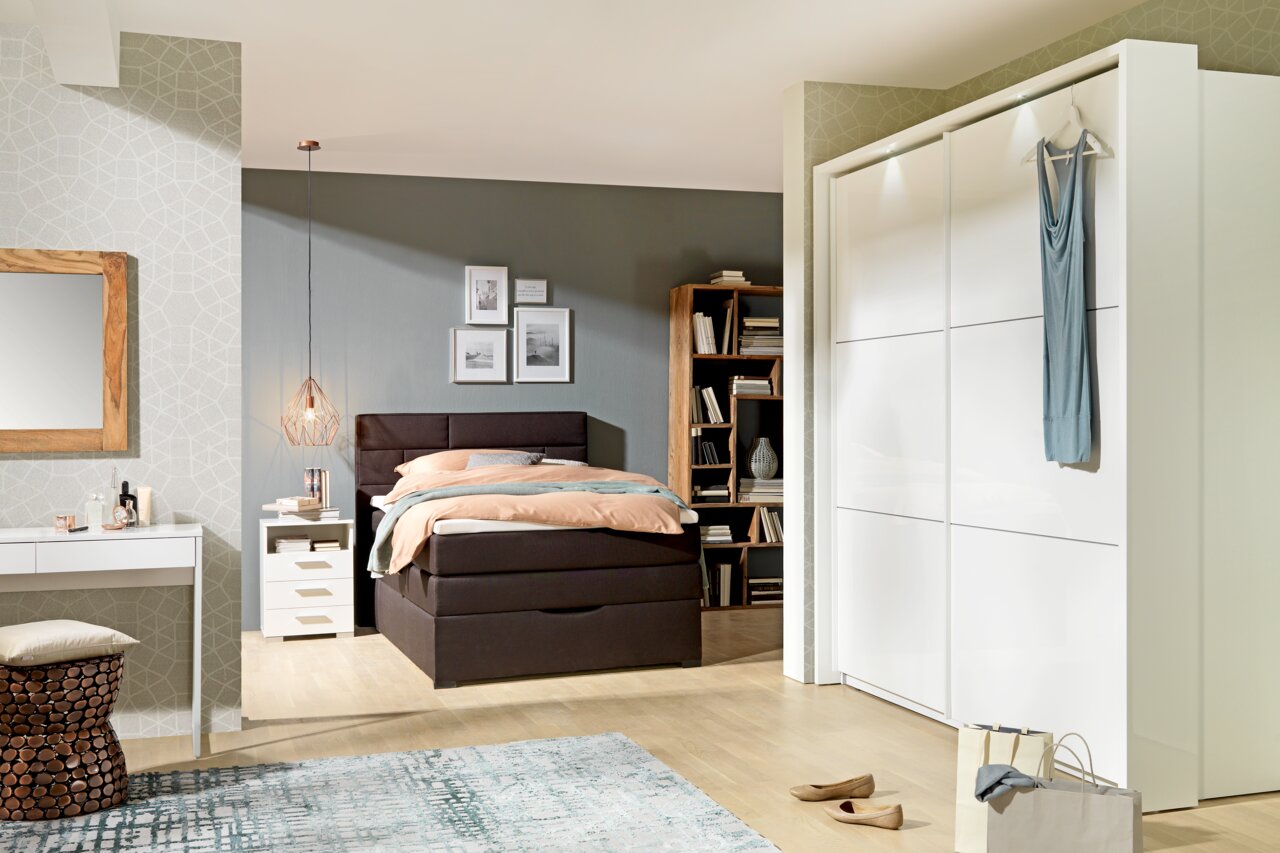 Moderner, weißer Schwebetürenschrank mit zwei Türen, frontal fotografiert, in einem stilvoll eingerichteten Schlafzimmer.