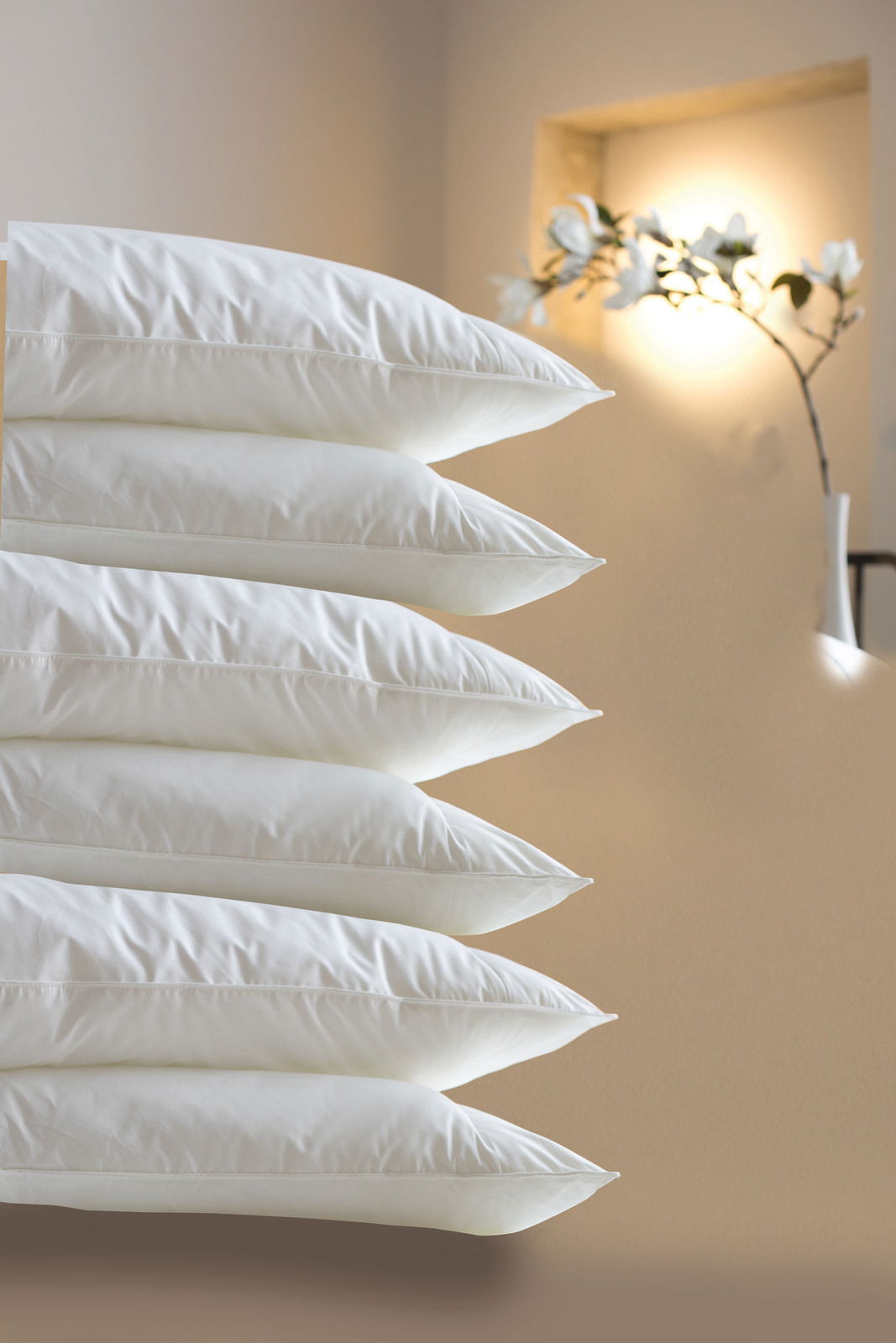 Centa Star Kopfkissen VITAL PLUS Stapel von weißen Kopfkissen in Seitenansicht vor einem dezent beleuchteten Hintergrund mit Blumen.