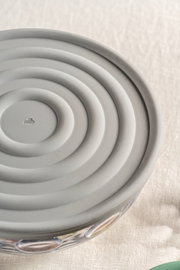 Grauer Silikondeckel mit konzentrischen Kreisen, von oben betrachtet, auf einer Glasschüssel.