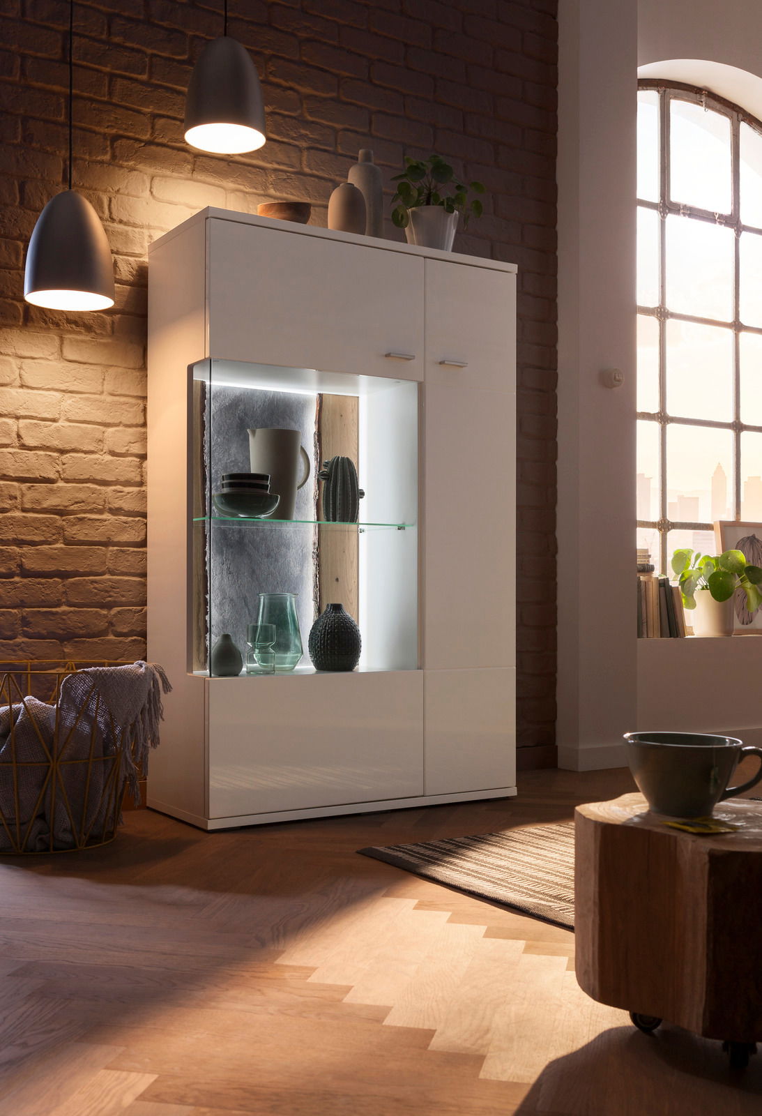 Modernes Highboard mit Glasvitrine, beleuchtet, in einem gemütlichen Wohnzimmer, seitliche Perspektive.