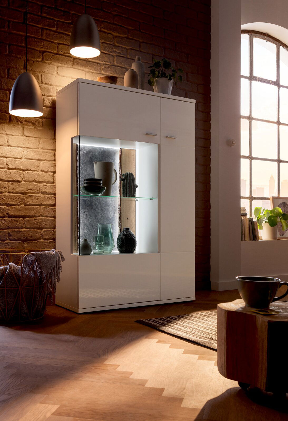 Modernes Highboard mit Glasvitrine, beleuchtet, in einem gemütlichen Wohnzimmer, seitliche Perspektive.