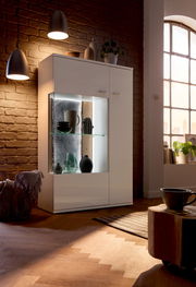 Modernes Highboard mit Glasvitrine, beleuchtet, in einem gemütlichen Wohnzimmer, seitliche Perspektive.