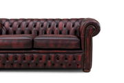 Nahaufnahme eines klassischen, dunkelroten Chesterfield-Sofas mit Knopfheftung und Armlehne von der rechten Seite.