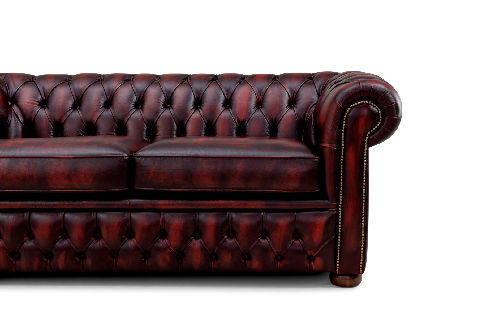 Close-up van een klassieke, donkerrode Chesterfield-bank met knopenbekleding en armleuning, gezien vanaf de rechterkant.