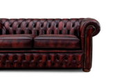 Close-up van een klassieke, donkerrode Chesterfield-bank met knopenbekleding en armleuning, gezien vanaf de rechterkant.