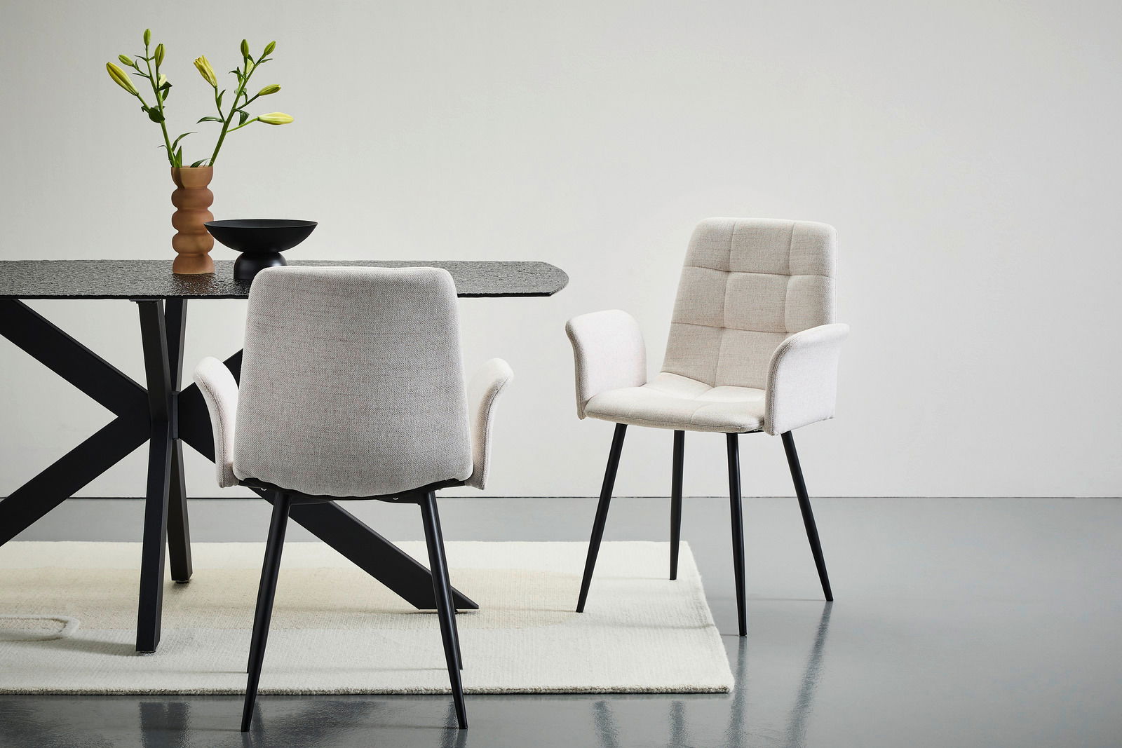 Stylife Armlehnstuhl JEFF Zwei moderne Armlehnstühle in hellem Stoff mit schwarzen Beinen, einer von vorne und einer von hinten, neben einem Tisch mit dekorativer Vase.