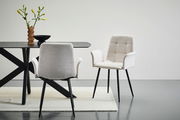 Zwei moderne Armlehnstühle in hellem Stoff mit schwarzen Beinen, einer von vorne und einer von hinten, neben einem Tisch mit dekorativer Vase.