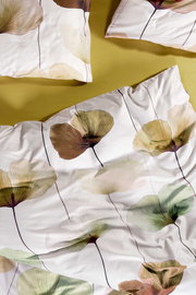 Draufsicht auf weiße Bettwäsche mit großflächigem, zartem Blätter-/Blumenprint in Grün-, Beige- und Brauntönen, mit Kissenbezügen auf gelbem Untergrund