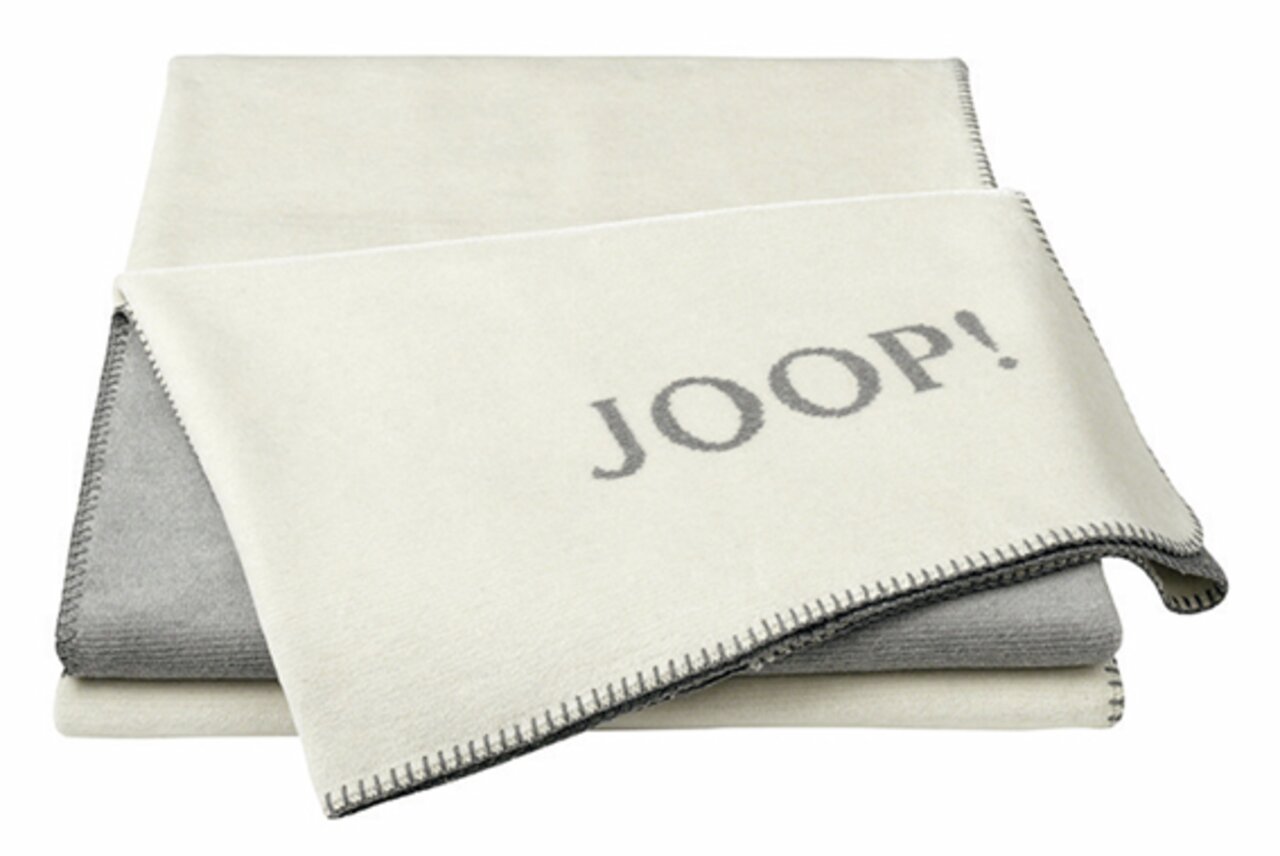 JOOP! Woon- en knuffeldeken MELANGE-DOUBLEFACE Beige und graue Decke mit dem Schriftzug 'JOOP!' in einer gefalteten Perspektive.