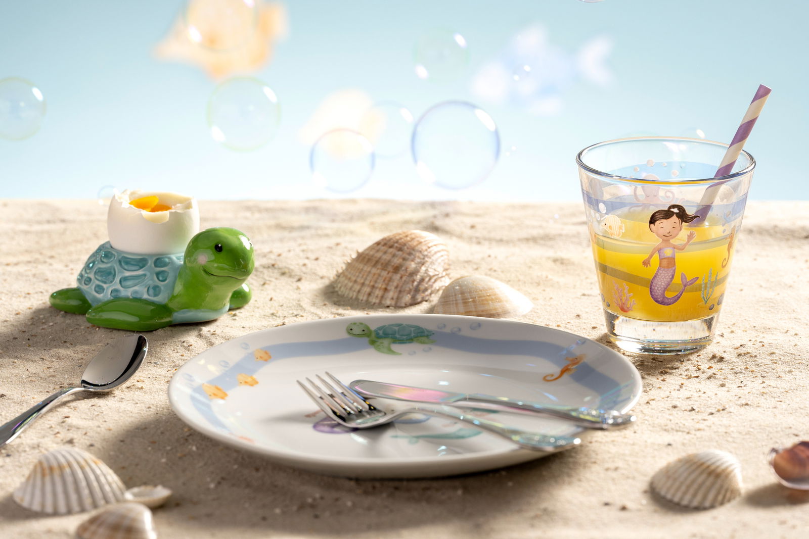 Eierbecher in Form einer Schildkröte mit einem gekochten Ei, auf einem sandigen Untergrund mit Muscheln, aus der Seitenperspektive fotografiert.