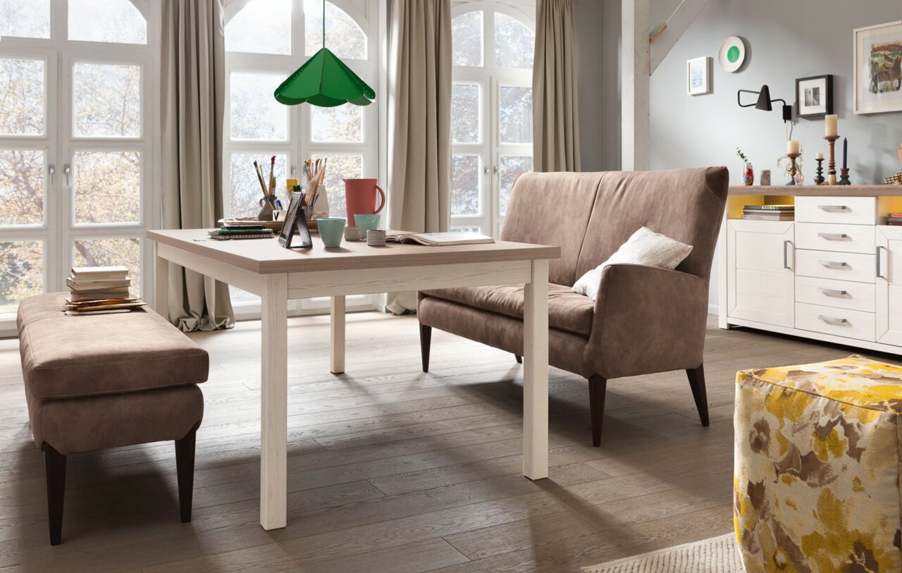 Set one by Musterring Esstisch SET ONE YORK Moderner Esstisch in einem hellen Raum mit großen Fenstern, flankiert von einer Bank und einem Sofa, seitliche Perspektive.