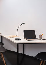 Moderne LED-Schreibtischleuchte auf einem Schreibtisch neben einem Laptop, aus seitlicher Perspektive fotografiert.