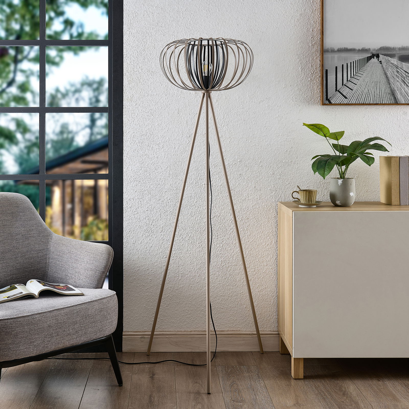 Moderne Stehleuchte mit dreibeinigem Stativ und dekorativem Lampenschirm in einem stilvollen Wohnzimmer, seitliche Perspektive.