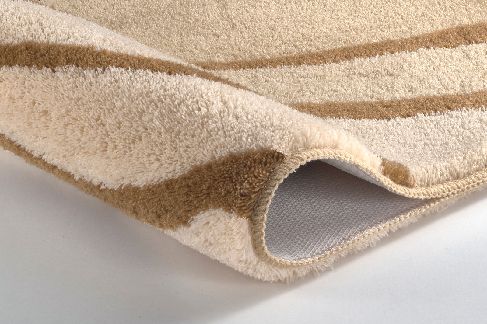 Kleine Wolke Badteppich JULIE Nahaufnahme eines beigen und braunen Badteppichs mit weicher Textur und rutschfester Unterseite, perspektivisch von der Seite aufgenommen.