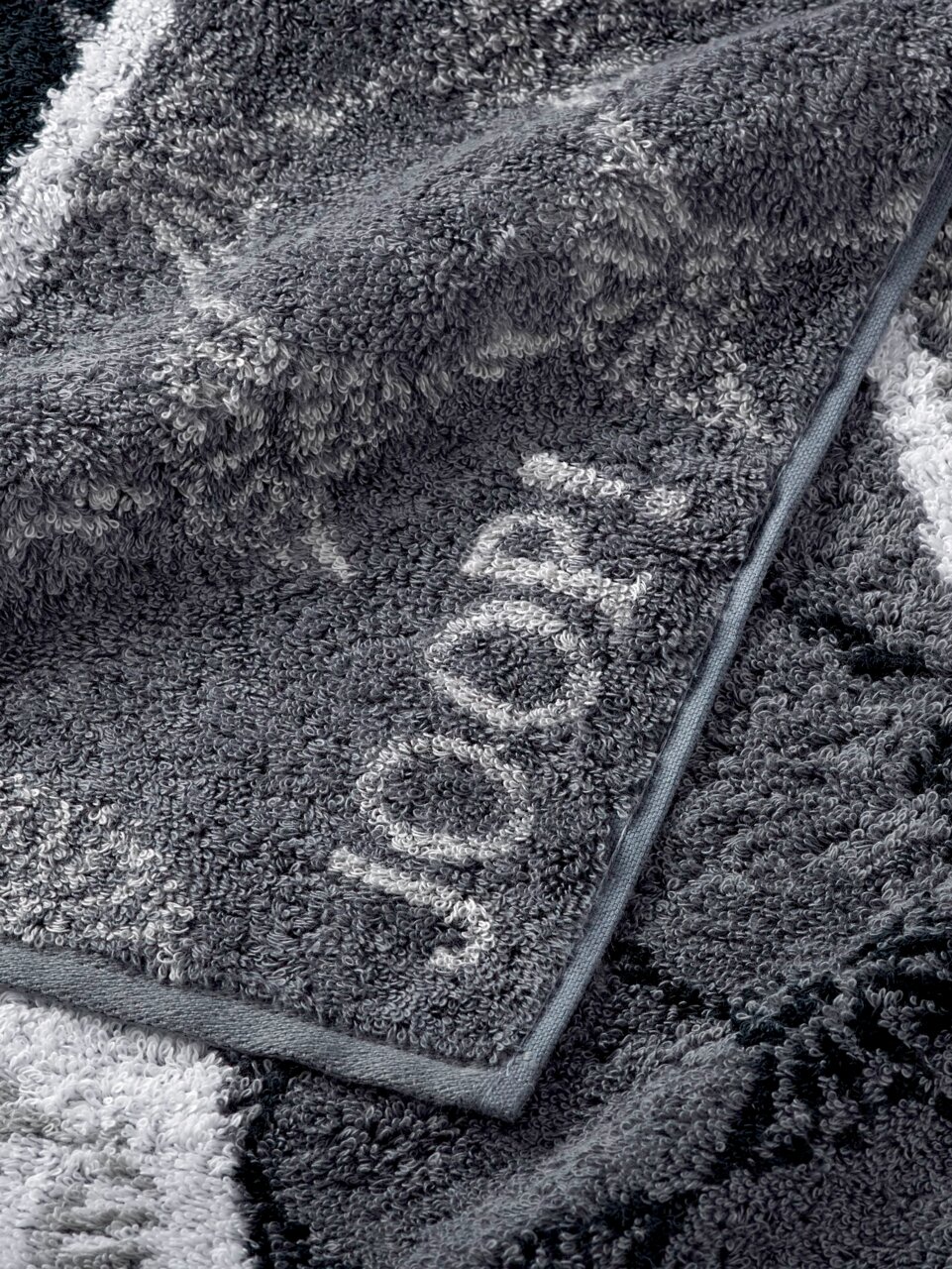 JOOP! Handtuch SIGNATURE Graues Handtuch mit eingewebtem Schriftzug, Nahaufnahme der Textur und Kante.