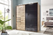Moderner Kleiderschrank mit Holz- und Glaselementen, frontal fotografiert in einem hellen Schlafzimmer.