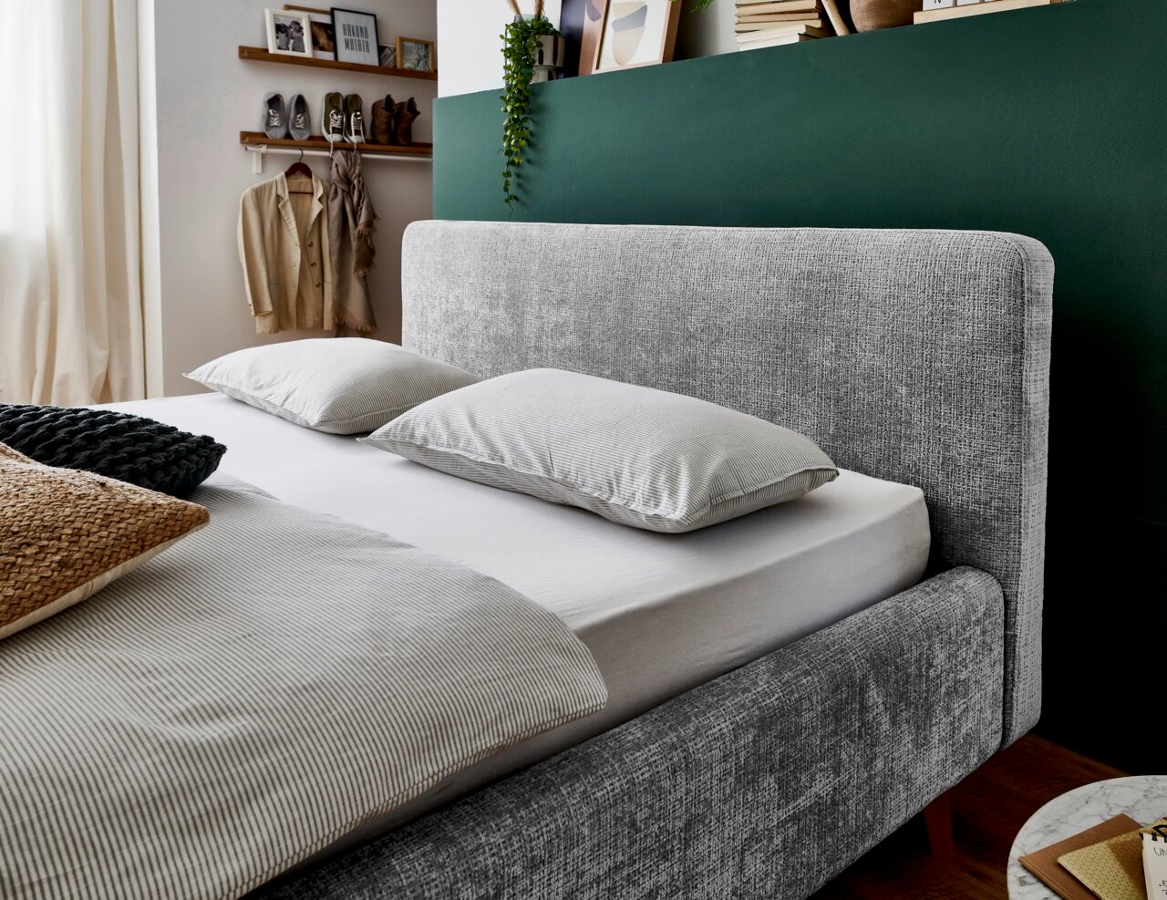 Grijs bedframe met bekleding in een gezellige slaapkamer, zijaanzicht