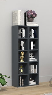 Dunkelgraues, hohes Regal mit mehreren offenen Fächern, gefüllt mit Büchern und Deko (u. a. goldene Figur, Glasflakon, Skulptur); oben liegen Bücher und eine Vase mit rosa Hortensien – Frontalansicht im Wohnraum.