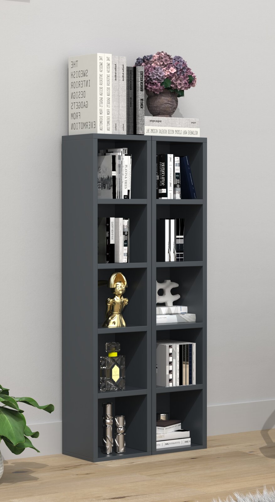 Dunkelgraues, hohes Regal mit mehreren offenen Fächern, gefüllt mit Büchern und Deko (u. a. goldene Figur, Glasflakon, Skulptur); oben liegen Bücher und eine Vase mit rosa Hortensien – Frontalansicht im Wohnraum.