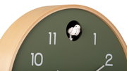 Nahaufnahme einer runden Wanduhr mit grünem Zifferblatt und hellem Holzrahmen, die einen Kuckucksvogel bei der 12-Uhr-Position zeigt.
