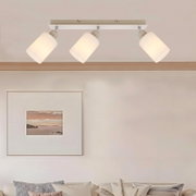 Witte plafondspot met drie verstelbare cilindervormige lampenkappen op een rechthoekige plafondplaat, warm wit licht; frontale aanblik licht van onderen in een woonkamer