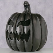 Schwarzer Halloween-Kürbis (Jack-o’-Lantern) mit grimmigem, ausgeschnittenem Gesicht und gezacktem Mund, frontal aus leicht niedriger Perspektive fotografiert vor hellem Hintergrund.