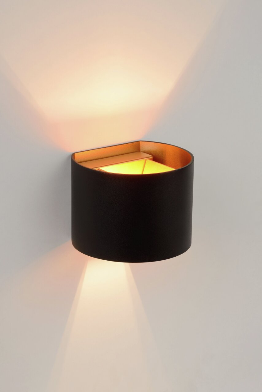 Moderne Wandleuchte XIO in schwarzem Zylinderdesign mit warmem Licht, seitliche Perspektive.