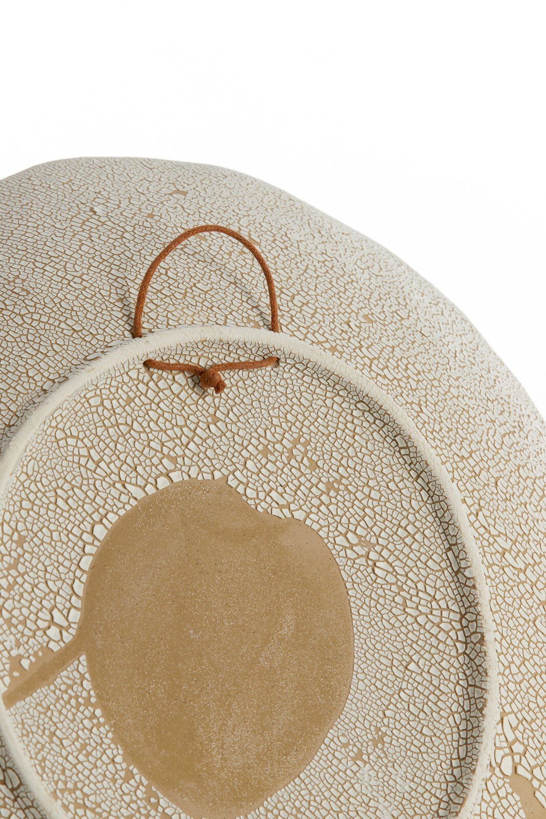 Nahaufnahme eines dekorativen Ornaments mit rissiger Textur und einem zentralen, runden Muster. Das Ornament hat eine beige und weiße Farbgebung und ist mit einer Schlaufe zum Aufhängen versehen.