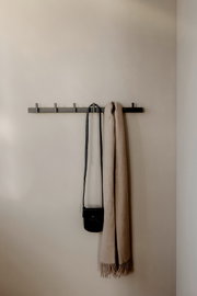 Schwarze, minimalistische Wandgarderobe mit mehreren Haken, daran hängen eine kleine schwarze Umhängetasche und ein beiger Schal; frontale Ansicht.