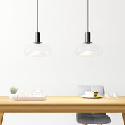 Zwei moderne Hängeleuchten mit transparentem Glasschirm über einem Esstisch, seitliche Perspektive