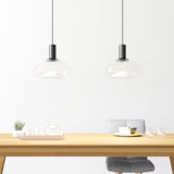 Zwei moderne Hängeleuchten mit transparentem Glasschirm über einem Esstisch, seitliche Perspektive