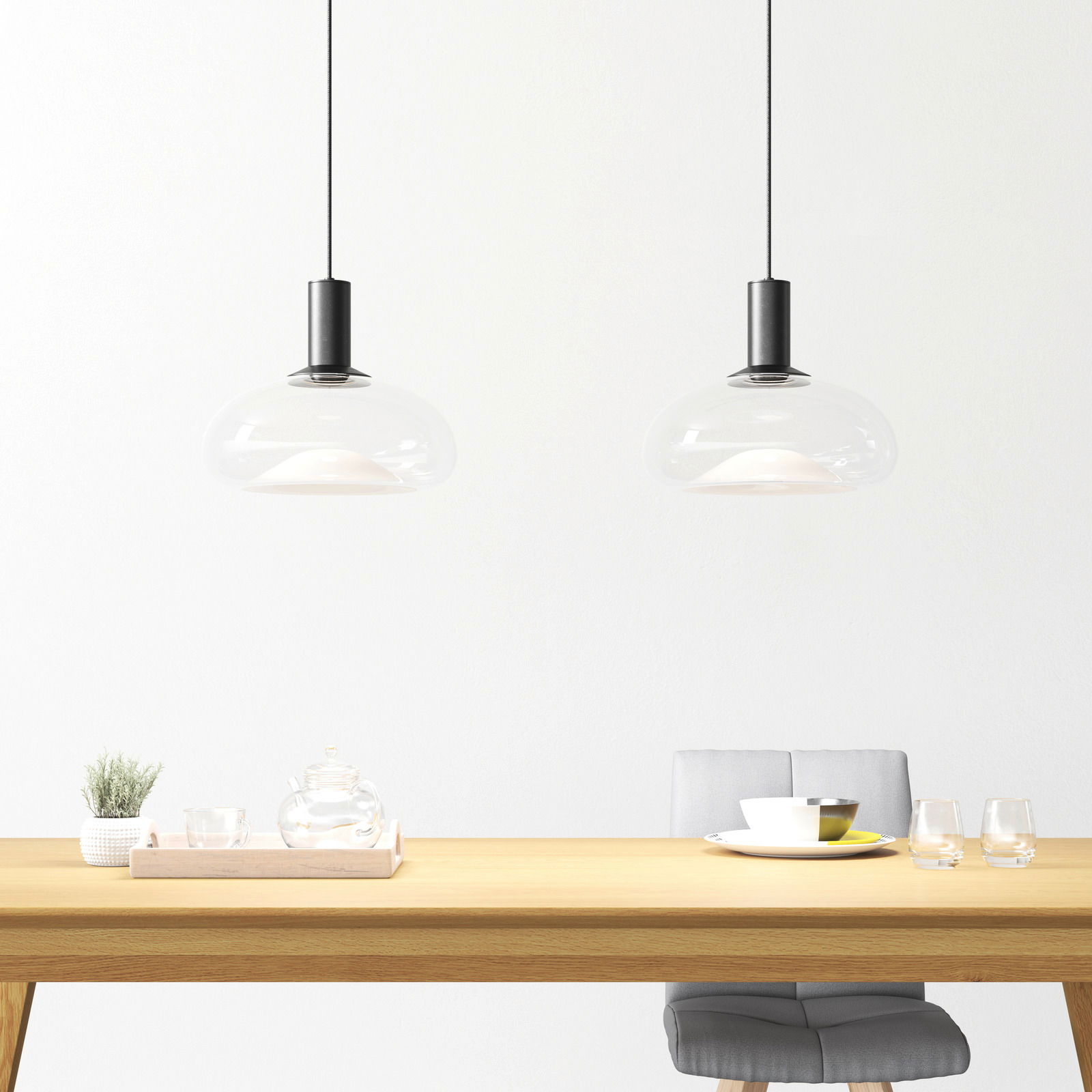 Zwei moderne Hängeleuchten mit transparentem Glasschirm über einem Esstisch, seitliche Perspektive