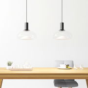 Zwei moderne Hängeleuchten mit transparentem Glasschirm über einem Esstisch, seitliche Perspektive