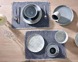 Vogelperspektive auf einen gedeckten Tisch mit einem flachen Teller, Schalen und Tassen in einem eleganten, blauen Design auf blauen Platzdeckchen.