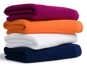 Vier gefaltete Handtücher in verschiedenen Farben, von oben nach unten: lila, orange, weiß und dunkelblau, seitliche Perspektive.