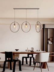 Vooraanzicht van een moderne drievoudige hanglamp met warme lichtbronnen en decoratieve metalen ringen boven een stijlvolle eettafel.