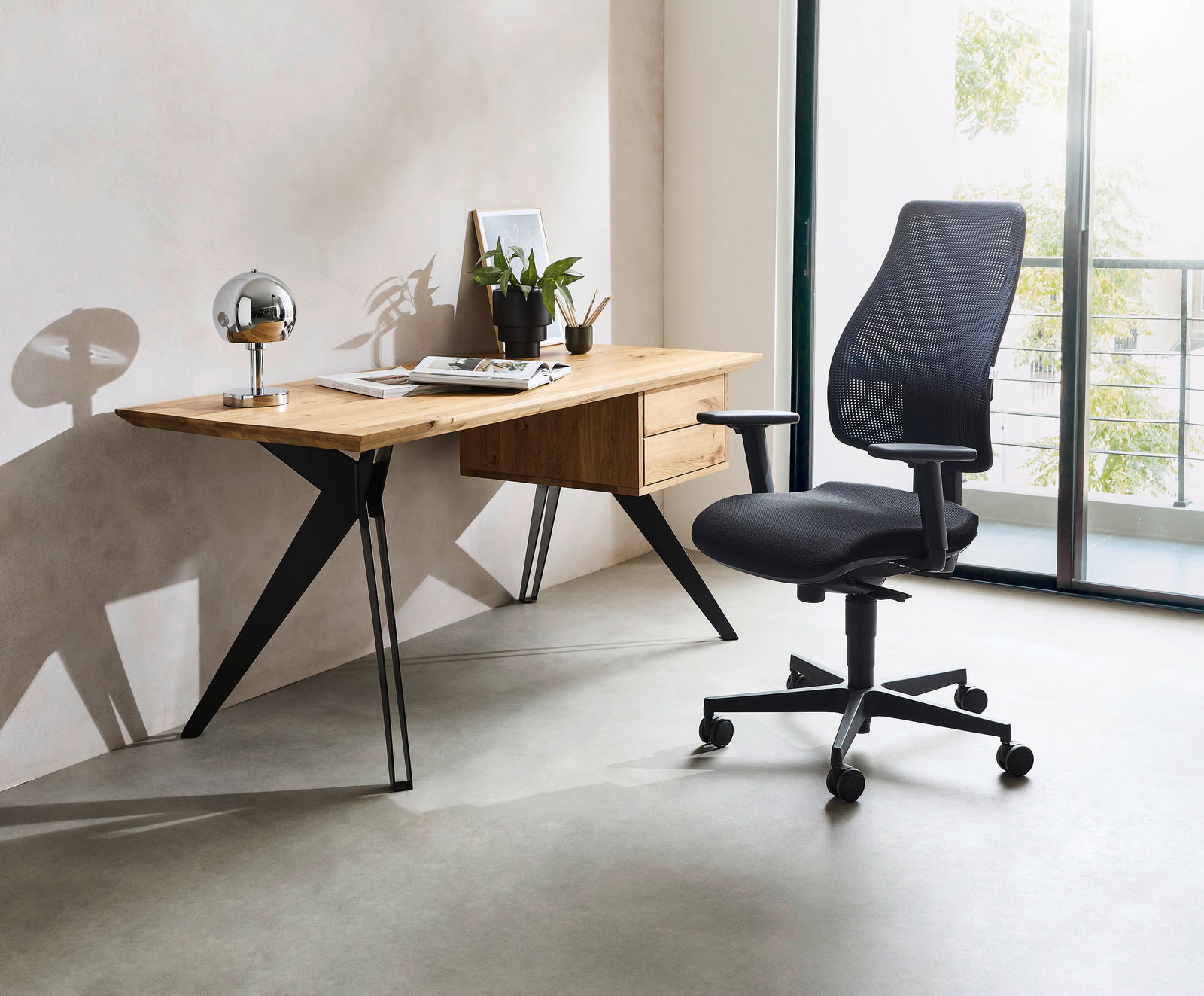 Moderner Schreibtisch aus Holz mit schwarzen Metallbeinen, dekoriert mit einer Lampe, Pflanzen und Büchern, seitliche Perspektive.