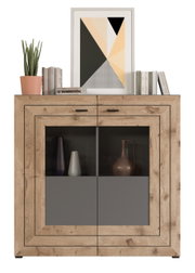 Frontale Ansicht eines modernen Highboards aus Holz mit zwei Türen, dekoriert mit Büchern, einer Pflanze und einem geometrischen Kunstwerk.