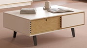 Moderner rechteckiger Couchtisch in Beige mit Holzschublade und schwarzen schrägen Beinen, auf der Tischplatte liegen Bücher und eine Tasse, fotografiert aus leicht erhöhter Frontperspektive.