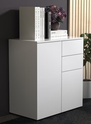 Modernes weißes Sideboard/Kommode mit glatten Fronten und drei Schubladen rechts, links eine Tür; oben dekoriert mit Büchern und Blumentopf, perspektivische Ansicht schräg von vorne links.