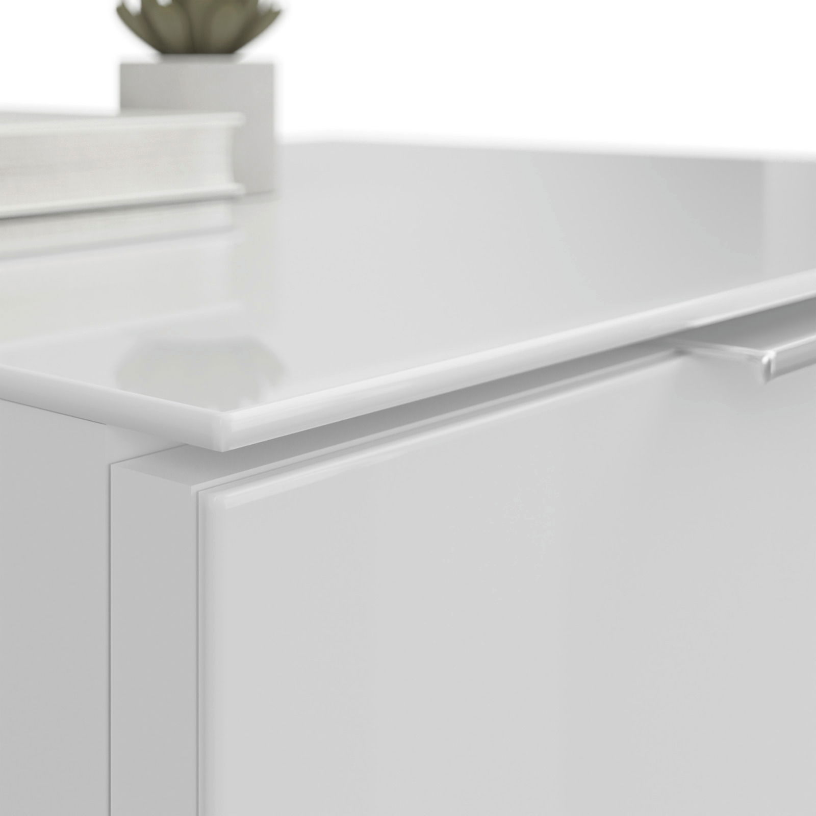 Nahaufnahme einer weißen Nachtkommode mit glänzender Oberfläche, auf der ein Buch und eine kleine Pflanze stehen. Perspektive von oben.