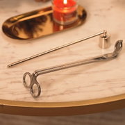 Silbernes Kerzenpflege-Set mit Dochtschere und Kerzenlöscher, aus schräger Nahperspektive auf einem eleganten Marmortisch mit brennender Duftkerze arrangiert