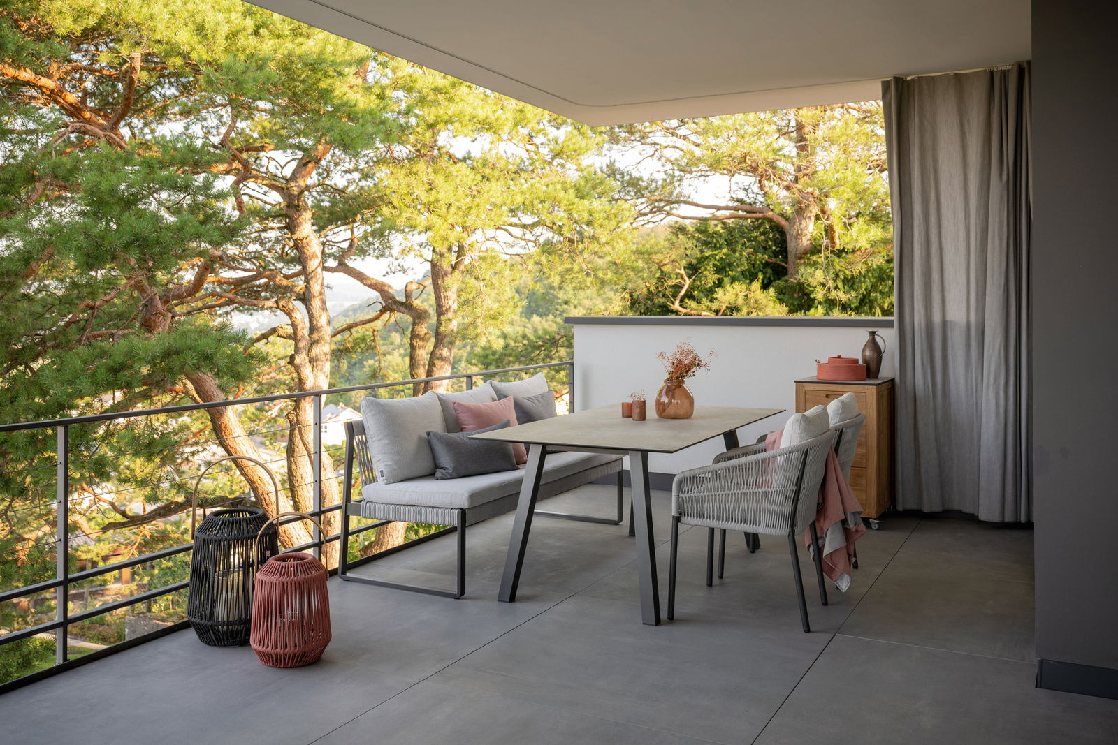 Stern Tuintafel INTERNO Moderner Gartentisch auf einem Balkon mit Blick auf Bäume, umgeben von stilvollen Stühlen und Dekorationen, seitliche Perspektive.