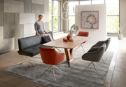 Moderner Esstisch aus Holz mit V-förmigem Gestell, umgeben von stilvollen Stühlen in einem eleganten Esszimmer mit großen Fenstern. Perspektive: seitlich.
