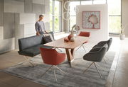 Moderner Esstisch aus Holz mit V-förmigem Gestell, umgeben von stilvollen Stühlen in einem eleganten Esszimmer mit großen Fenstern. Perspektive: seitlich.
