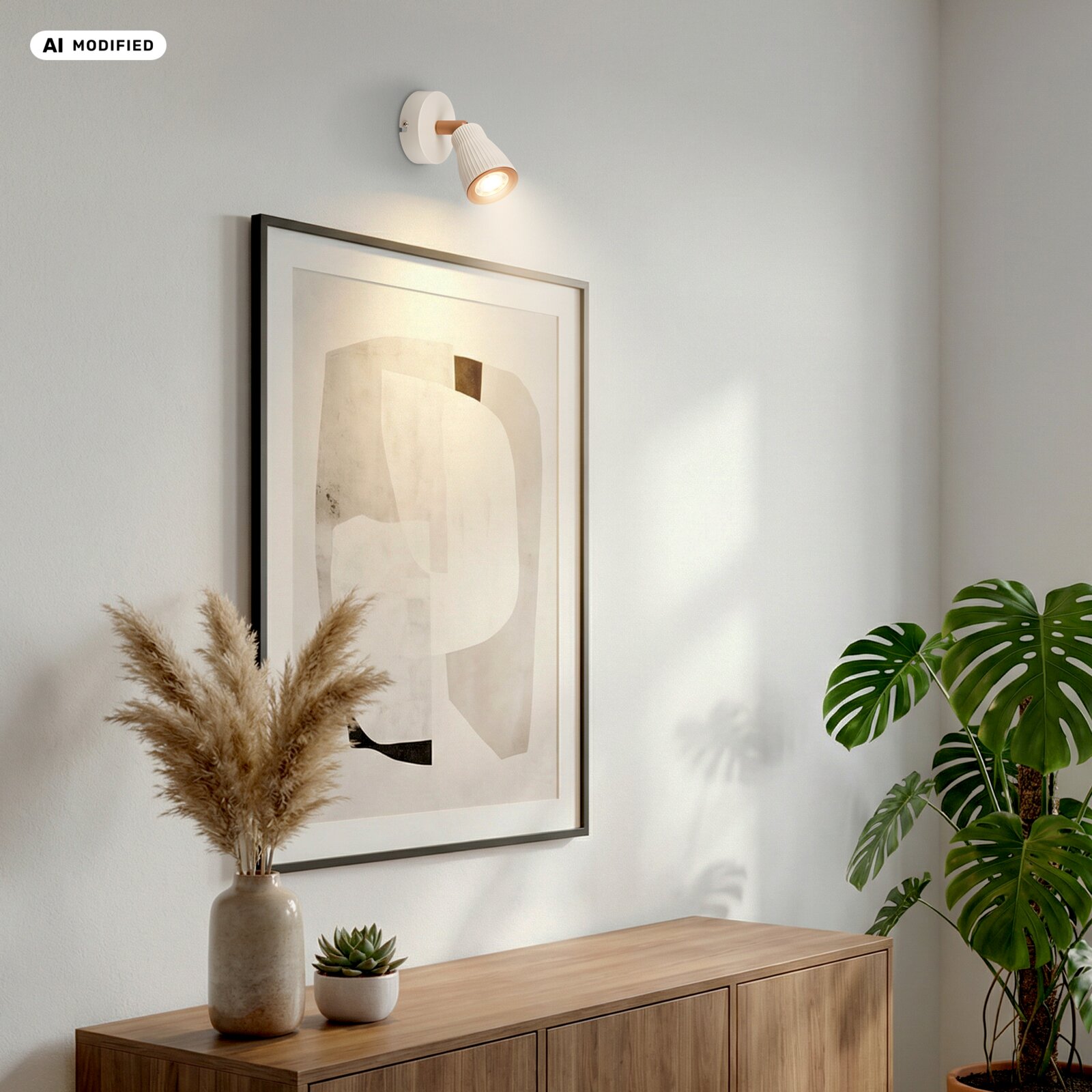 Weiße Wandspot-Leuchte mit geriffeltem Schirm und warmem Licht über einem gerahmten abstrakten Bild an heller Wand, seitliche Perspektive von links im Wohnraum mit Holz-Sideboard und Pflanzen.