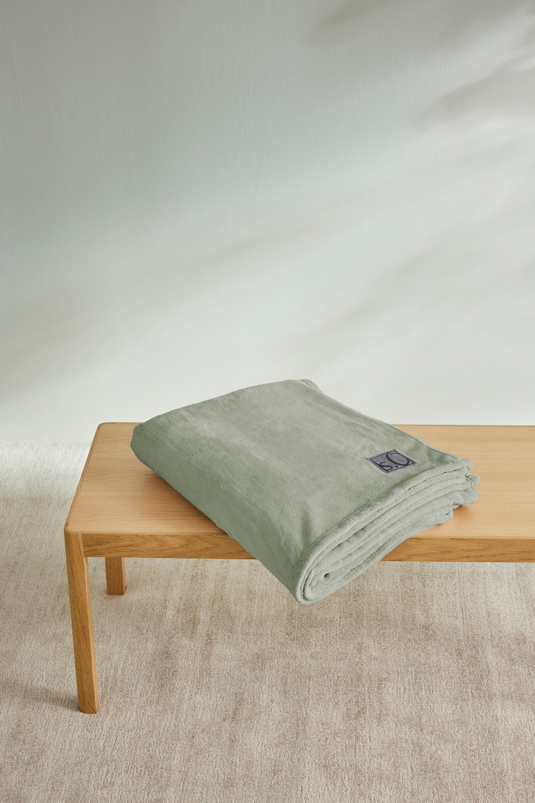 Gefaltete, hellgrüne Kuscheldecke von s.Oliver auf einem Holztisch, seitliche Perspektive.