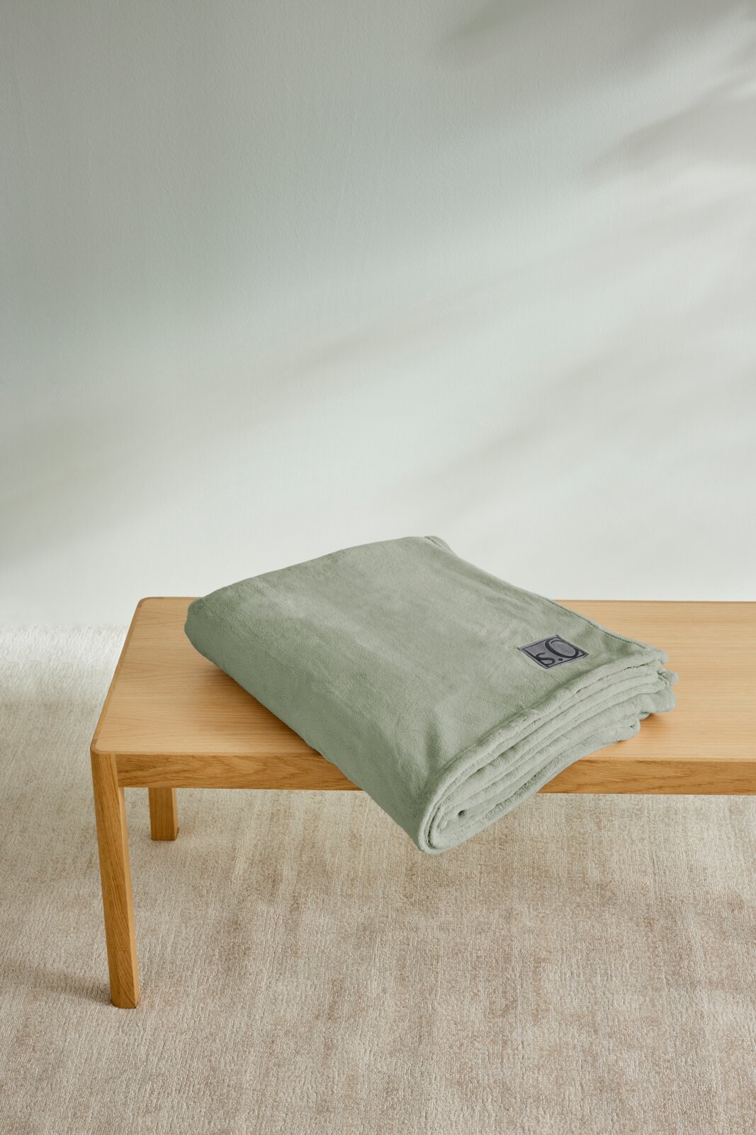 Gefaltete, hellgrüne Kuscheldecke von s.Oliver auf einem Holztisch, seitliche Perspektive.